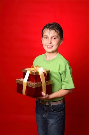 simsearch:400-03961239,k - A smiling boy carrying gifts wrapped in golden ribbon on a red background, Photographie de stock - Aubaine LD & Abonnement, Code: 400-03942888