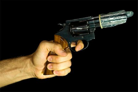 Male hand holding a revolver with a condom on it. Black background. Photographie de stock - Aubaine LD & Abonnement, Code: 400-03967103