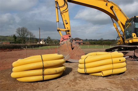 Two rolls of yellow plastic drainage piping on a building site, with part of an excavator to the rear. Foto de stock - Super Valor sin royalties y Suscripción, Código: 400-03968447