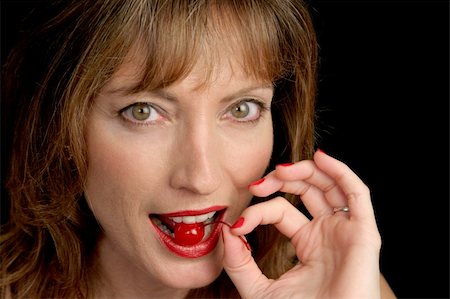 A closeup of a beautiful woman's face as she bites into a juicy red cherry. Photographie de stock - Aubaine LD & Abonnement, Code: 400-03971645