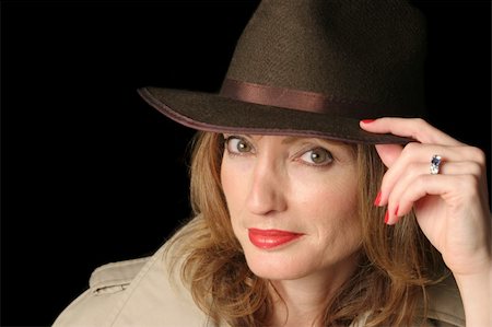 A beautiful woman in a smiling in a hat and trenchcoat over a black background.  Possible marital role playing. Photographie de stock - Aubaine LD & Abonnement, Code: 400-03971662