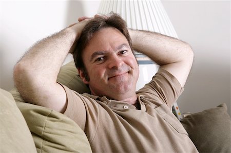 A handsome, friendly man relaxing at home with his hands behind his head. Photographie de stock - Aubaine LD & Abonnement, Code: 400-03972305