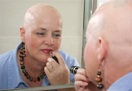 A woman bald from a health problem putting on makeup in the mirror. Stockbilder - Microstock & Abonnement, Bildnummer: 400-03972393