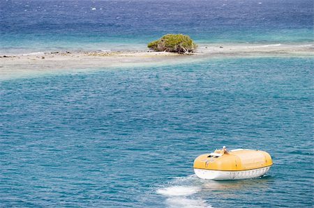 A cruiseship lifeboat, on training exercises during a cruise, approaches a desert island with just one scrub tree on it. The island, on a coral reef, is surrounded by the blue ocean. Foto de stock - Super Valor sin royalties y Suscripción, Código: 400-03983590