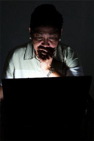 Frightened looking elderly Asian woman looking at the computer screen in the dark with the light coming from the computer Stock Photo - Budget Royalty-Free & Subscription, Code: 400-03995910