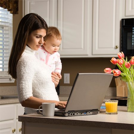 Mother holding baby  and typing on laptop computer in kitchen. Stock Photo - Budget Royalty-Free & Subscription, Code: 400-03998294