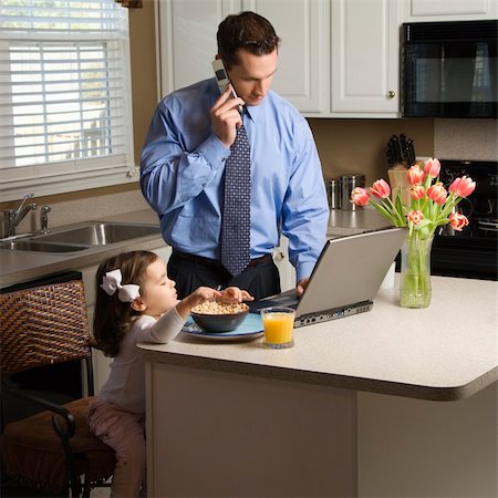 Caucasian father in suit talking on cellphone and using laptop computer with daughter eating breakfast in kitchen. Stock Photo - Budget Royalty-Free & Subscription, Code: 400-03998297