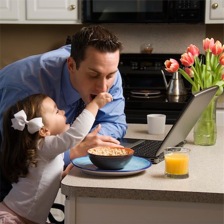 family eating computer - Caucasian father in suit using laptop computer with daughter feeding him breakfast in kitchen. Stock Photo - Budget Royalty-Free & Subscription, Code: 400-03998300