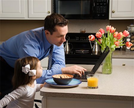 Caucasian father in suit using laptop computer with daughter eating breakfast in kitchen. Stock Photo - Budget Royalty-Free & Subscription, Code: 400-03998301