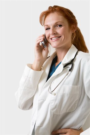 simsearch:400-04704005,k - Female attractive doctor with red hair tied back in a ponytail wearing white lab coat smiling while talking on a cell phone Stock Photo - Budget Royalty-Free & Subscription, Code: 400-03992273