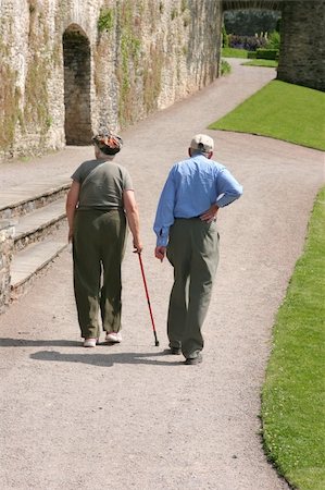 simsearch:400-05746567,k - Elderly man and woman walking together along a path with the female holding a walking stick and the man holding his back as if in pain. Stock Photo - Budget Royalty-Free & Subscription, Code: 400-03992444