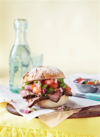 steak roll bun - Steak Sandwich on Bun With Tomatoes and Onions on Table Stock Photo - Premium Royalty-Free, Code: 600-06397661