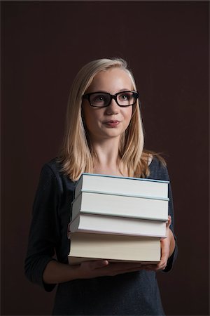 Portrait of Blond, Teenage Girl wearing Eyeglasses and Carrying Stack of Books, Studio Shot on Black Background Stock Photo - Premium Royalty-Free, Code: 600-06438957