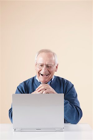 Senior Man Sitting at Table looking at Laptop Computer Laughing, Studio Shot on Beige Background Stock Photo - Premium Royalty-Free, Code: 600-06438983