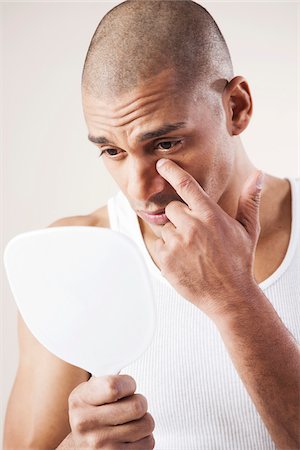 Man Looking at his Face in a Mirror in Studio with White Background Photographie de stock - Premium Libres de Droits, Code: 600-06485947