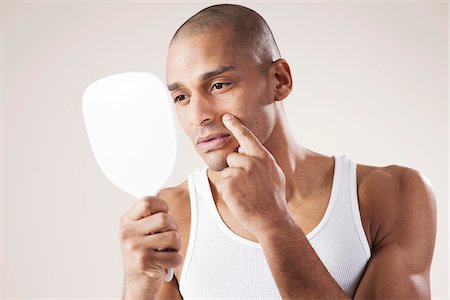 Man Looking at his Face in a Mirror in Studio with White Background Photographie de stock - Premium Libres de Droits, Code: 600-06485949