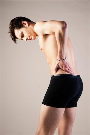 simsearch:600-06505868,k - Young Man in Boxer Briefs Standing Hunched with Hands on Back in Studio Stock Photo - Premium Royalty-Free, Code: 600-06486005