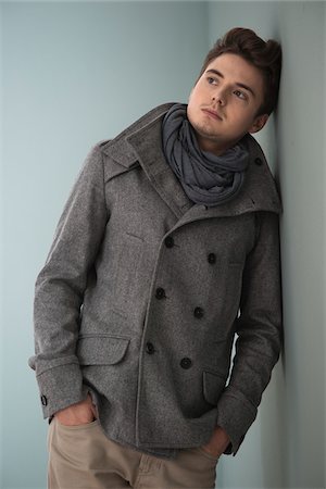 Portrait of Young Man wearing Grey Scarf and Jacket, Leaning against Wall, Studio Shot on Grey Background Stock Photo - Premium Royalty-Free, Code: 600-06486253