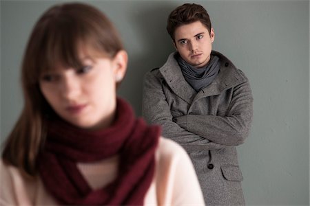 falling out - Portrait of Young Man Standing behind Young Woman, Looking at her Intensely, Studio Shot on Grey Background Stock Photo - Premium Royalty-Free, Code: 600-06486263
