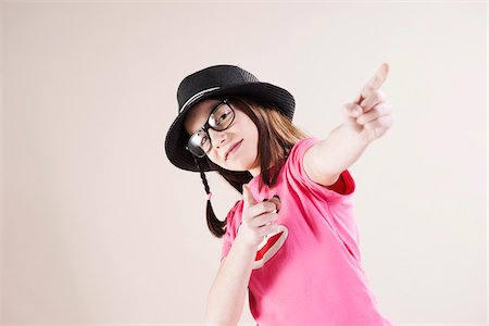 Portrait of Girl wearing Fedora and Horn-rimmed Eyeglasses, Pointing and Smiling at Camera, Studio Shot on White Background Photographie de stock - Premium Libres de Droits, Code: 600-06486284