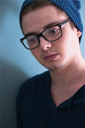 Close-up Portrait of Young Man wearing Woolen Hat and Horn-rimmed Eyeglasses, Looking Downward, Studio Shot on Blue Background Stockbilder - Premium RF Lizenzfrei, Bildnummer: 600-06486283