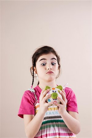 Portrait of Girl Looking Cross Eyed at Piggy Bank in Studio Stock Photo - Premium Royalty-Free, Code: 600-06486432