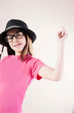 Portrait of Girl wearing Fedora and Horn-rimmed Eyeglasses, Smiling at Camera, Studio Shot Stock Photo - Premium Royalty-Free, Code: 600-06505874