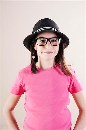 Portrait of Girl wearing Fedora and Horn-Rimmed Eyeglasses, Looking at Camera, Studio Shot Stock Photo - Premium Royalty-Free, Code: 600-06505873