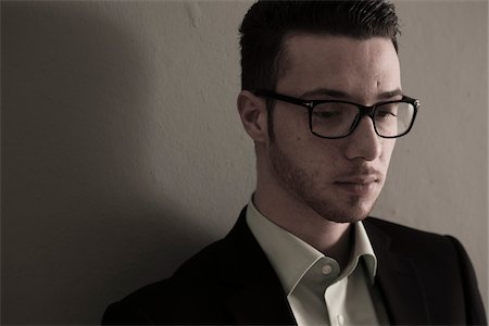 simsearch:700-07278870,k - Close-up Portrait of Young Man wearing Suit Jacket and Horn-rimmed Eyeglasses. Looking Downward, Absorbed in Thought, Studio Shot Stock Photo - Premium Royalty-Free, Code: 600-06505880