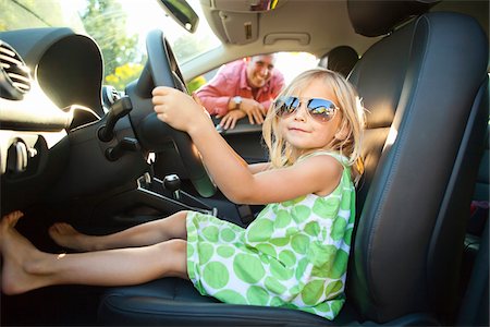 Portrait of little girl sitting in driver's seat of car, pretending to be old enough to drive as her smiling father watches on on a sunny summer evening in Portland, Oregon, USA Photographie de stock - Premium Libres de Droits, Code: 600-06531449