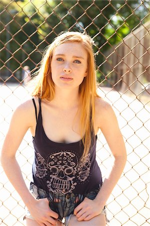 Portrait of young woman standing in front of chain link fence in park near the tennis court on a warm summer day in Portland, Oregon, USA Fotografie stock - Premium Royalty-Free, Codice: 600-06531456