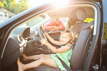 simsearch:600-06531430,k - Little girl sitting in driver's seat of car wearing seatbelt, pretending to be old enough to drive and showing she knows the importance of a seat belt as her smiling father watches on on a sunny summer evening in Portland, Oregon, USA Foto de stock - Sin royalties Premium, Código: 600-06531450