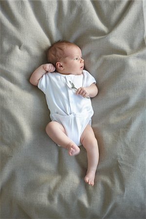 newborn baby girl in a white undershirt laying on a bed with a silver spoon in her hand, Ontario, Canada Stock Photo - Premium Royalty-Free, Code: 600-06531987