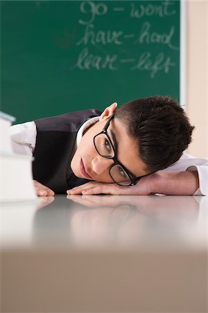 escuelas primarias - Boy with Head on Desk in front of Chalkboard in Classroom Foto de stock - Sin royalties Premium, Código: 600-06543541