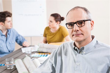 designer headshot - Portrait of Mature Businessman wearing Eyeglasses with Colleagues Meeting in the Background Photographie de stock - Premium Libres de Droits, Code: 600-06621004