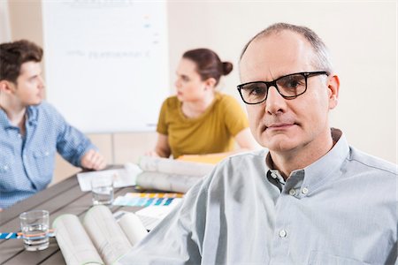 simsearch:600-06620994,k - Portrait of Mature Businessman wearing Eyeglasses with Colleagues Meeting in the Background Stock Photo - Premium Royalty-Free, Code: 600-06621004