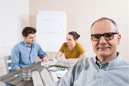 formlos - Portrait of Mature Businessman wearing Eyeglasses with Colleagues Meeting in the Background Photographie de stock - Premium Libres de Droits, Code: 600-06621005