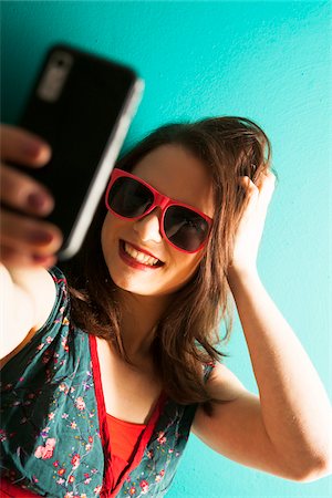 Portrait of Young Woman Wearing Sunglasses and Taking a Picture with a Cell Phone in Studio Stock Photo - Premium Royalty-Free, Code: 600-06645767