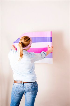 simsearch:600-06671767,k - Studio Shot of Young Woman Holding Wallpaper up to Wall Stock Photo - Premium Royalty-Free, Code: 600-06671781