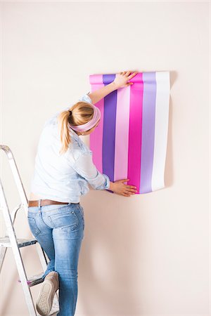 diy renovations - Studio Shot of Young Woman Holding Wallpaper up to Wall Photographie de stock - Premium Libres de Droits, Code: 600-06671783