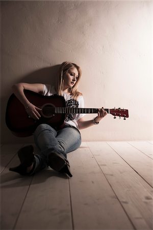 solitario - Young Woman Sitting on the Floor Playing Guitar in Studio Foto de stock - Sin royalties Premium, Código: 600-06701796