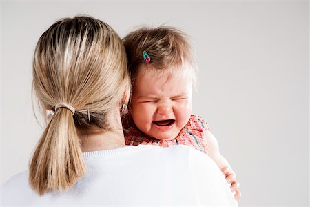 simsearch:600-06752395,k - Over the Shoulder View of Mother holding Crying Baby Girl, Studio Shot Foto de stock - Royalty Free Premium, Número: 600-06752383