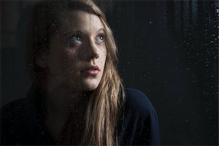 Portrait of young woman behind window, wet with raindrops, looking up Stock Photo - Premium Royalty-Free, Code: 600-06786758