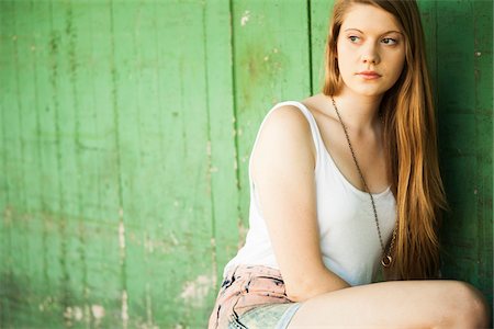 Portrait of young woman outdoors, crouching down by wall, looking to the side Stock Photo - Premium Royalty-Free, Code: 600-06786769