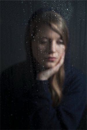 Portrait of young woman behind window, wet with raindrops, wearing hoodie Stock Photo - Premium Royalty-Free, Code: 600-06786762