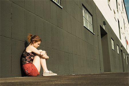 simsearch:700-03805279,k - Teenage girl sitting on ground and leaning against wall, looking downwards Stock Photo - Premium Royalty-Free, Code: 600-06786790