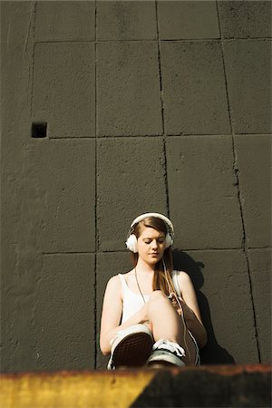 simsearch:600-06786784,k - Young woman sitting on ground, leaning against cement wall, listening to MP3 player Foto de stock - Sin royalties Premium, Código: 600-06786791