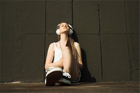 simsearch:600-06786784,k - Young woman sitting on ground, leaning against cement wall, listening to MP3 player Foto de stock - Sin royalties Premium, Código: 600-06786792