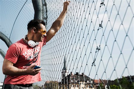 fenced - Mature man standing on outdoor basketball court holding MP3 player, Germany Stock Photo - Premium Royalty-Free, Code: 600-06786836