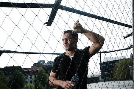 Mature man leaning against chain-link fence on outdoor basketball court, holding bottle of water, Germany Foto de stock - Sin royalties Premium, Código: 600-06786848